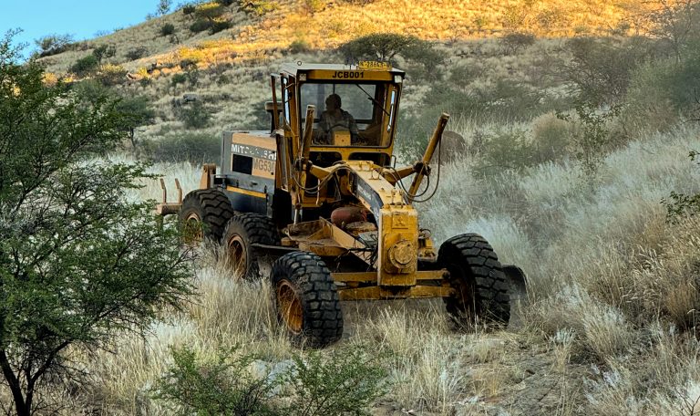 Ein gelber Grader der Namibian Wildlife Foundation (NWF) ebnet Wege im dichten Buschland des Khomashochlands