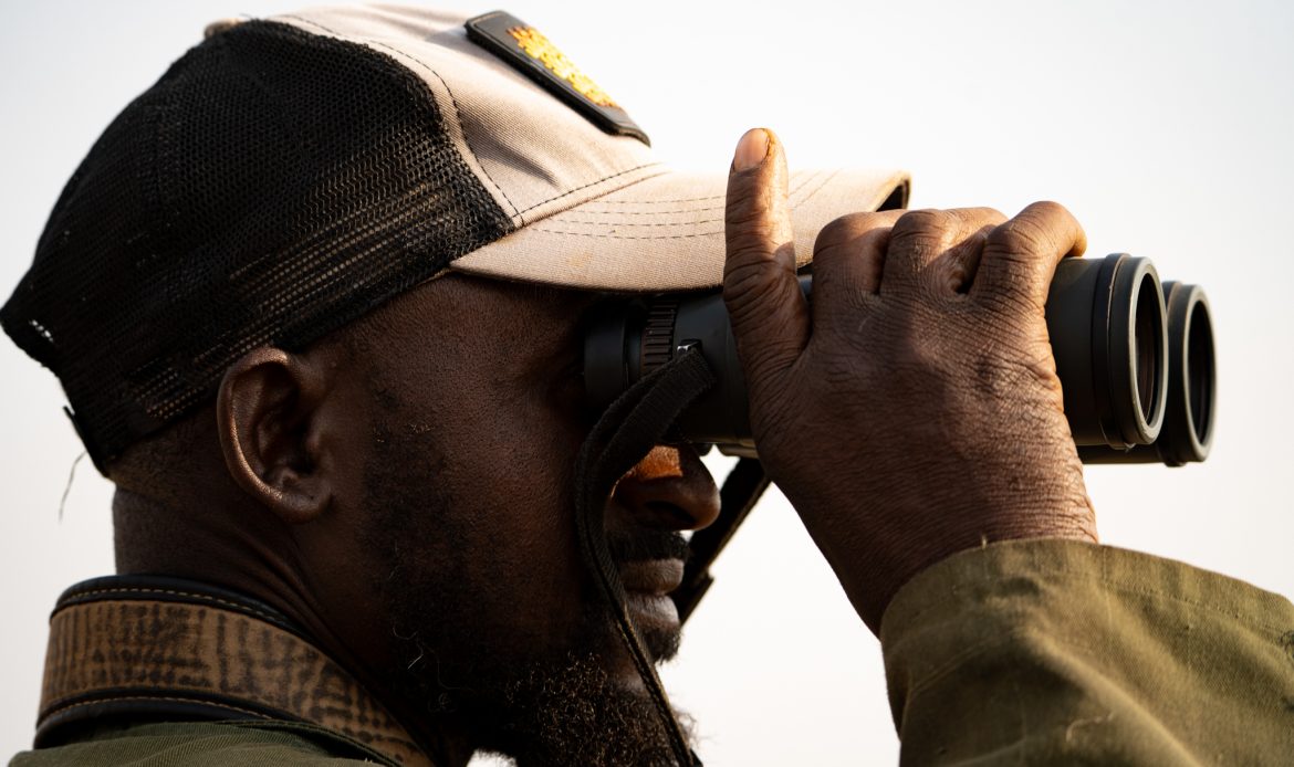 Ranger der Namibian Wildlife Foundation (NWF) beobachtet mit einem Fernglas das Gelände, um Wilderer frühzeitig zu erkennen und Wildtiere zu schützen.