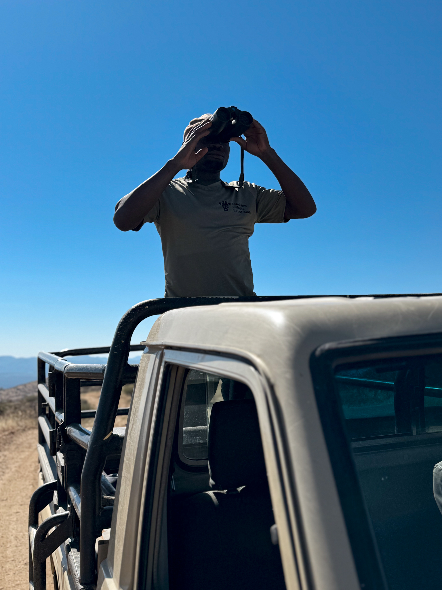Ranger der Namibian Wildlife Foundation (NWF) beobachtet das Schutzgebiet in Namibia mit einem Fernglas vom Fahrzeug aus.