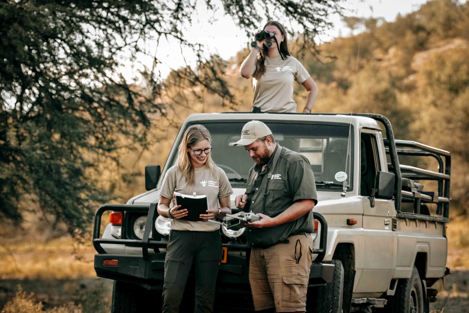 Team der Namibian Wildlife Foundation bei der Projektarbeit in Namibia mit Fahrzeug, Fernglas und Ausrüstung
