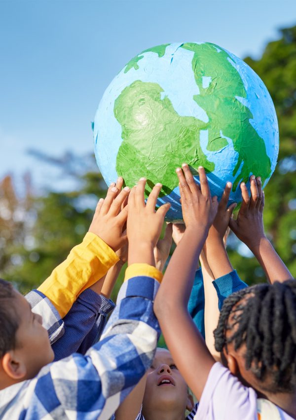 Children holding earth model for sustainable living concept Kinder stehen im Kreis und halten gemeinsam einen Globus in die Höhe.