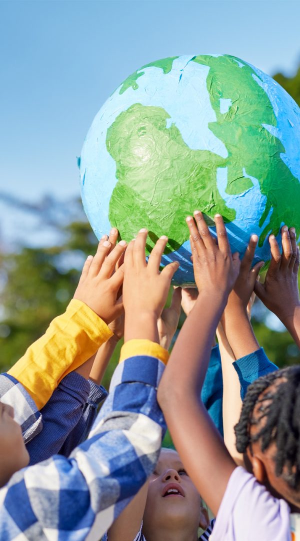 Children holding earth model for sustainable living concept Kinder stehen im Kreis und halten gemeinsam einen Globus in die Höhe.